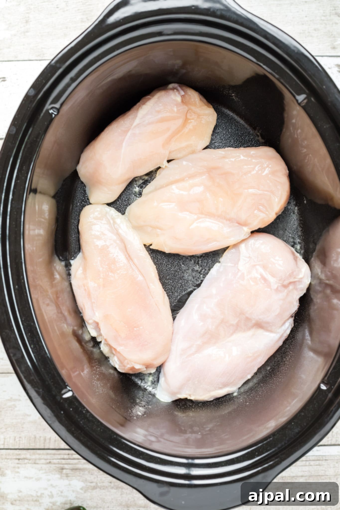 A slow cooker filled with the base ingredients for chicken enchilada soup, including chicken, tomatoes, and beans, before cooking.