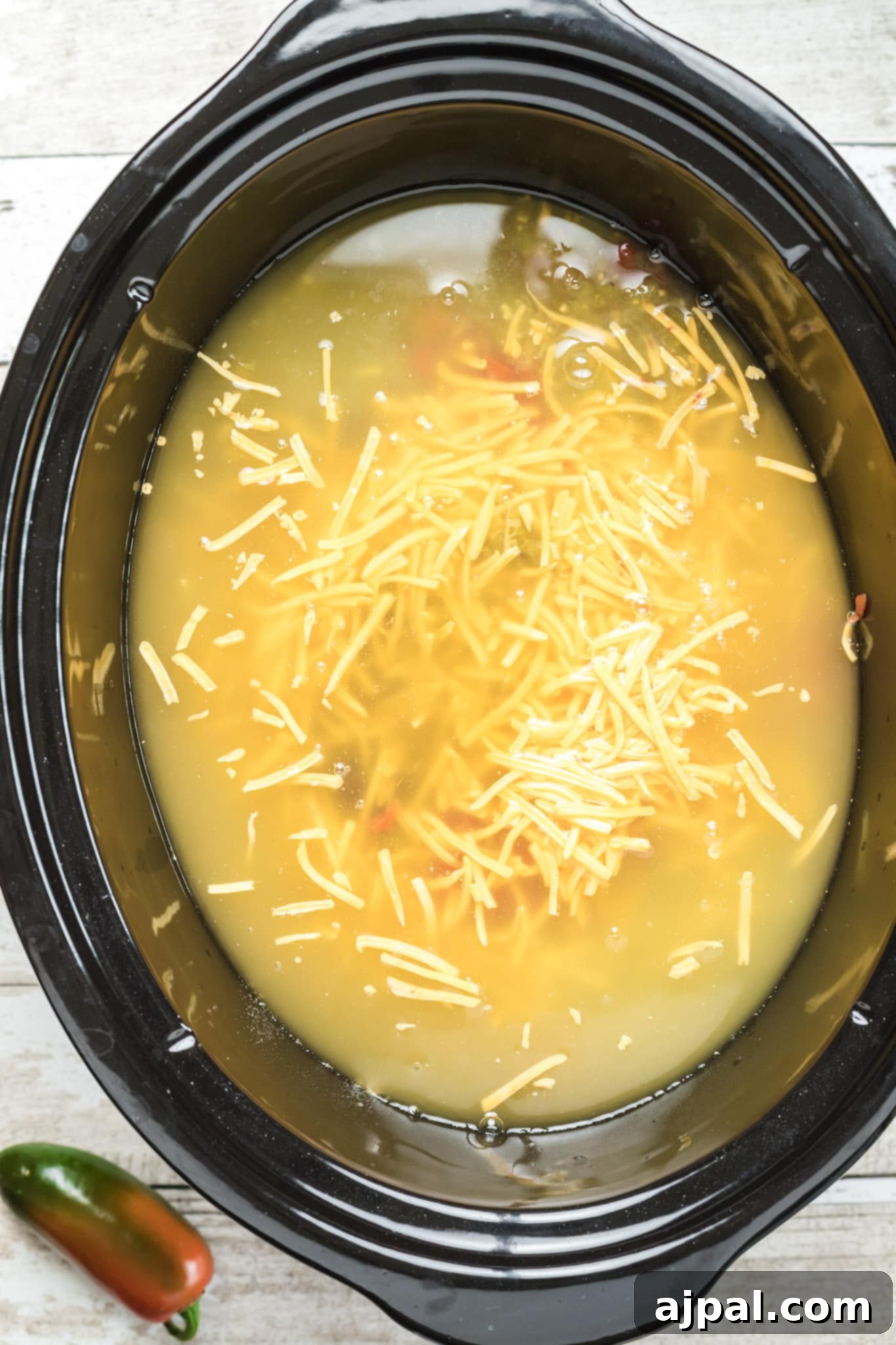 A slow cooker chicken enchilada soup with cheese and jalapeños, showing the creamy texture and rich ingredients.