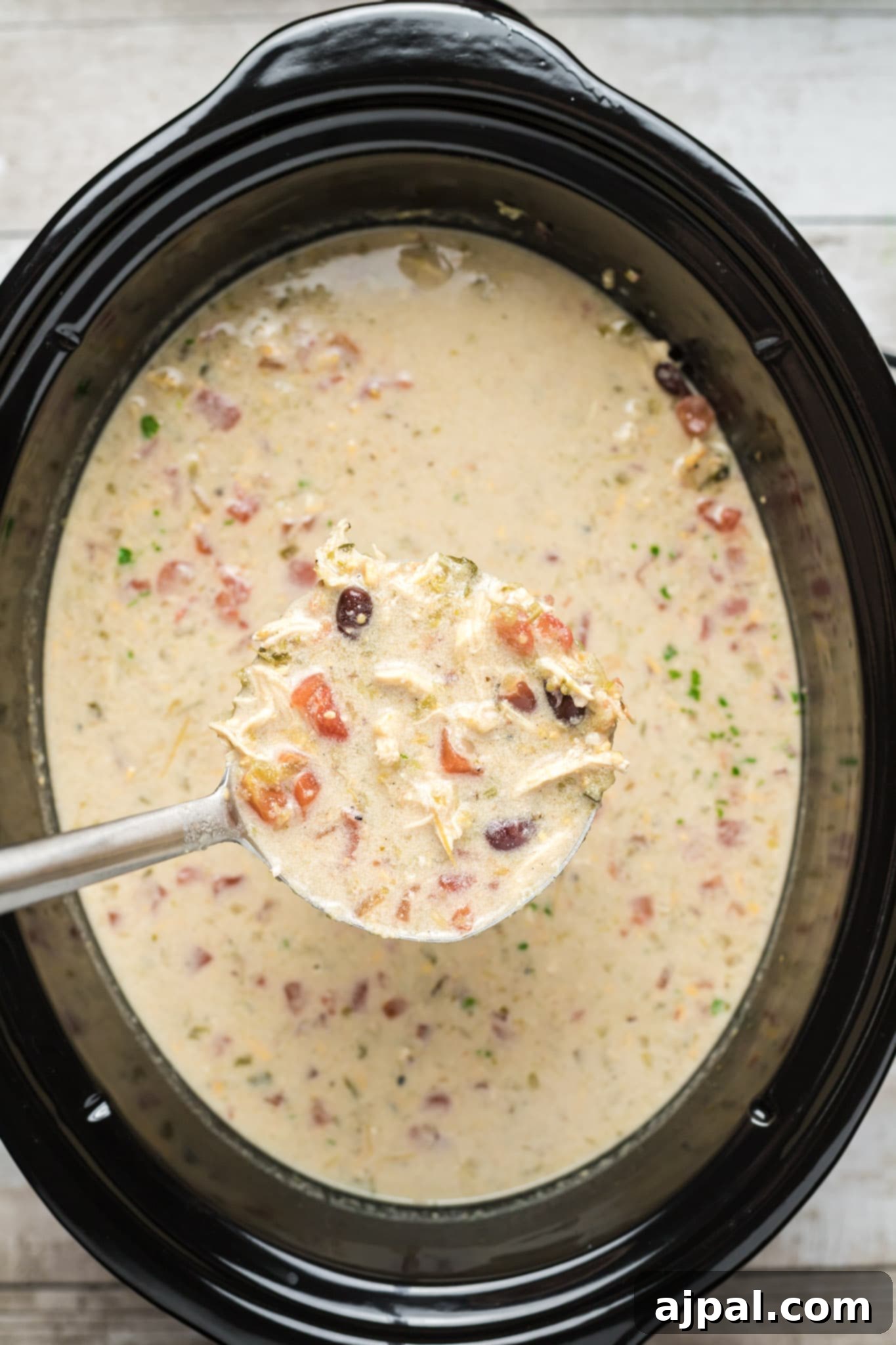A slow cooker enchilada soup recipe with a spoonful of soup in a crock pot, illustrating the final creamy consistency.
