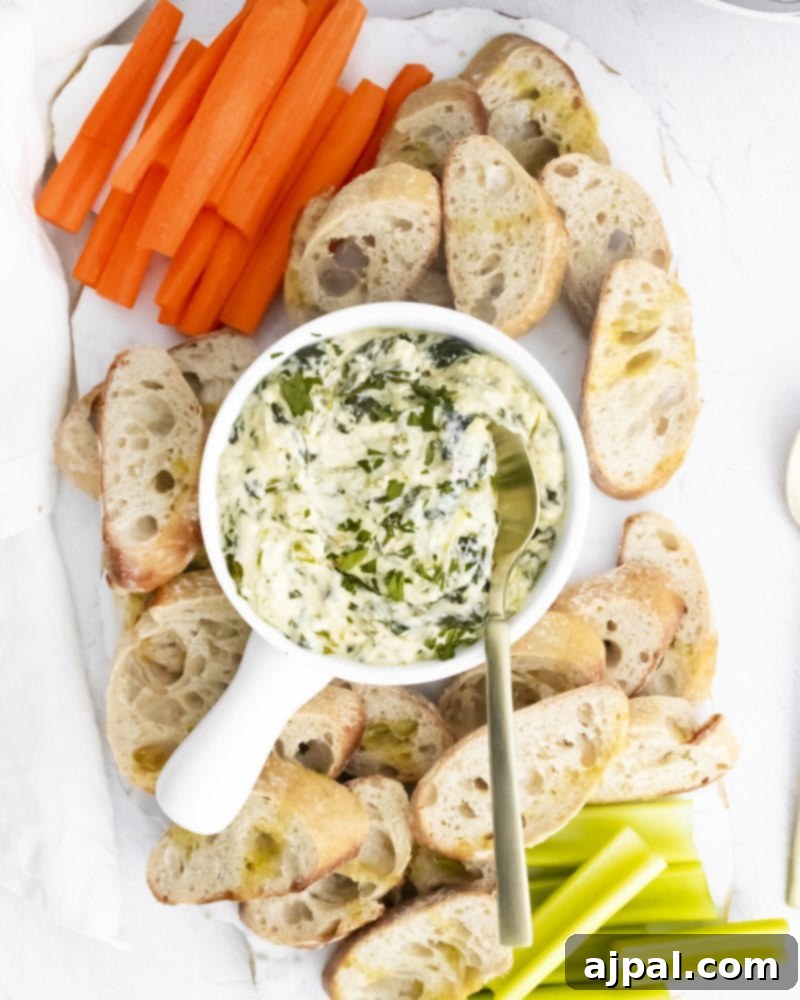 Creamy Instant Pot Spinach Dip 2 A vibrant bowl of Instant Pot spinach dip, garnished and surrounded by an assortment of fresh carrots, celery sticks, and slices of crusty bread, ready for dipping.