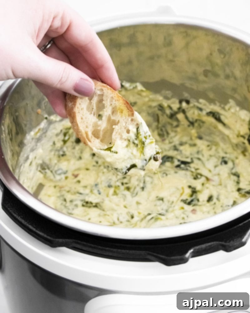 Creamy Instant Pot Spinach Dip 13 A hand dipping a slice of crusty bread into a rich, creamy spinach dip directly from the Instant Pot, highlighting its perfect texture.