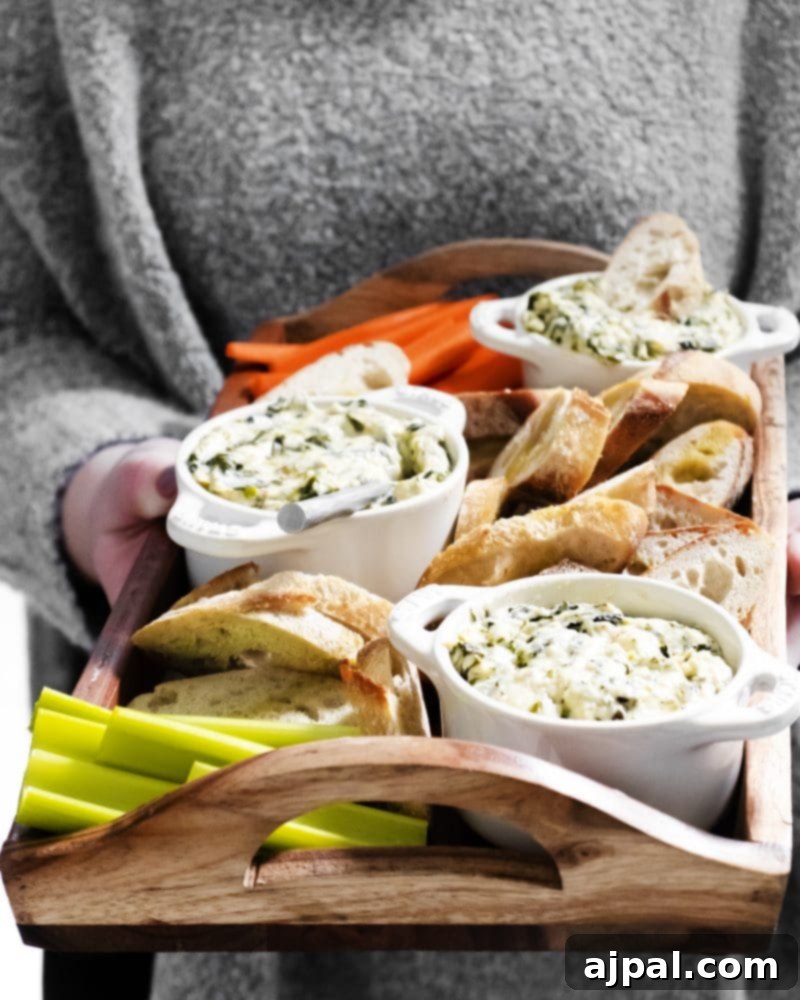 Creamy Instant Pot Spinach Dip 3 A person holding a tray featuring a bowl of Instant Pot spinach dip, surrounded by an appetizing display of bread slices and fresh carrot sticks, ready for serving.