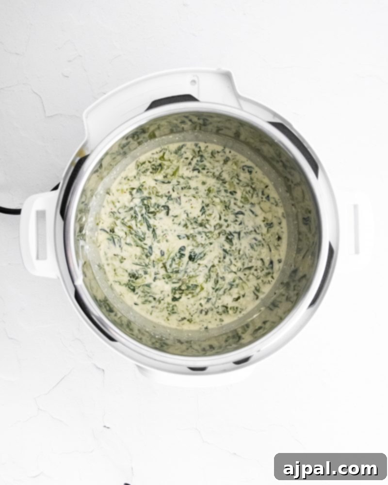 Creamy Instant Pot Spinach Dip 8 Spinach dip simmering in an Instant Pot, with fresh spinach visible.