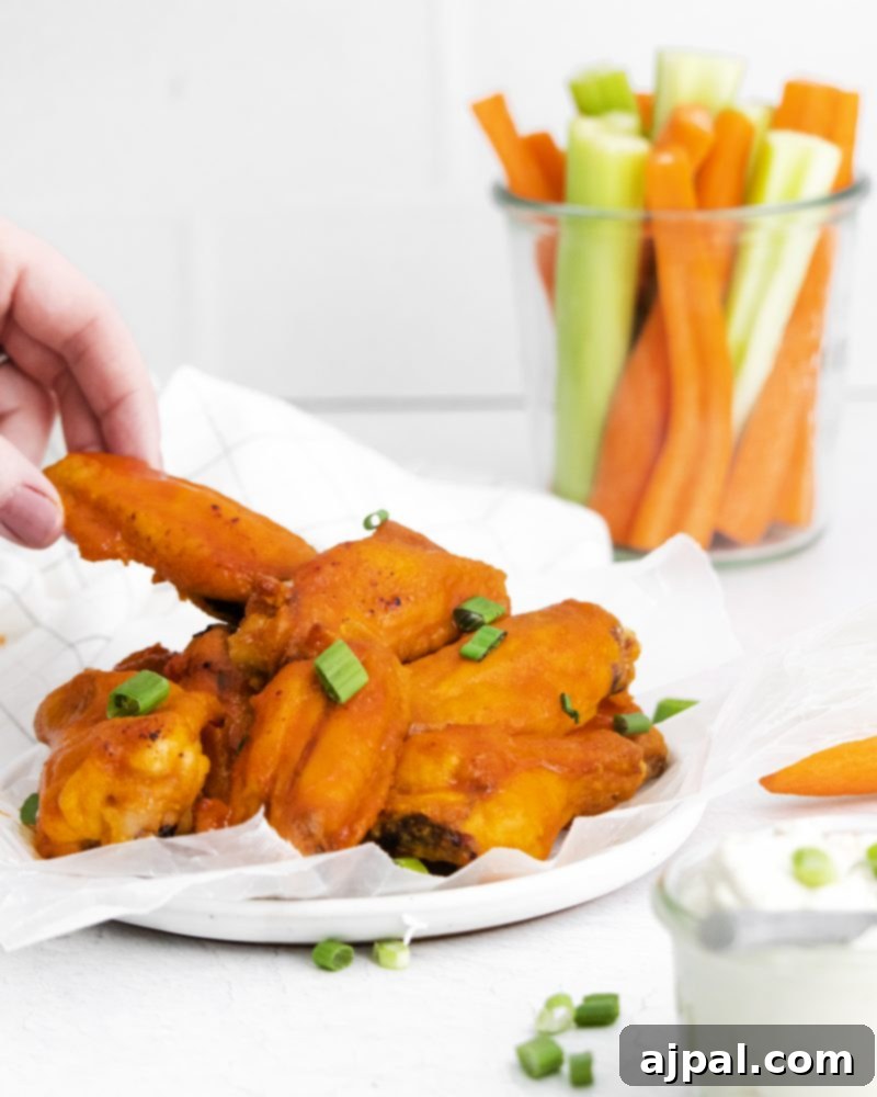 Sticky Sweet Buffalo Wings 5 A hand dipping a honey buffalo chicken wing into a bowl filled with crisp carrots and celery, a perfect pairing.