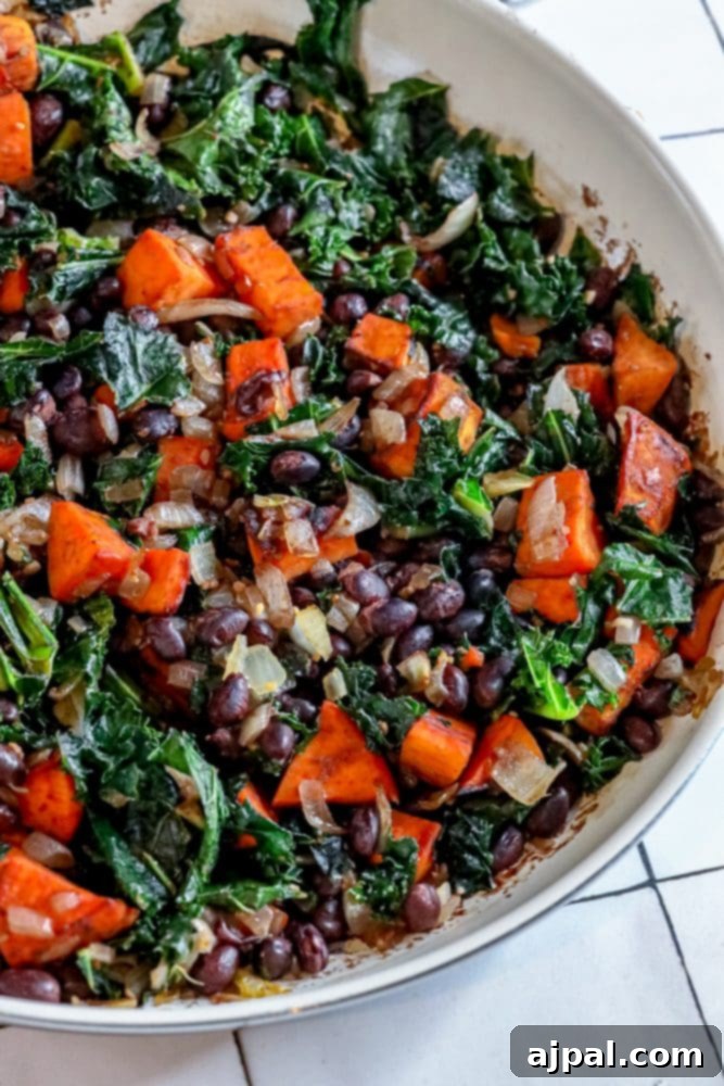 A generous serving of vegan sweet potato, kale, and black bean skillet in a bowl, highlighted with fresh herbs.