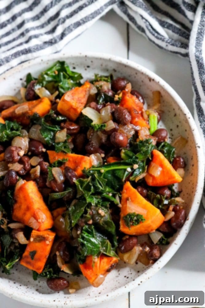A close-up of a vibrant sweet potato, kale, and black bean skillet in a white bowl, garnished with fresh cilantro.