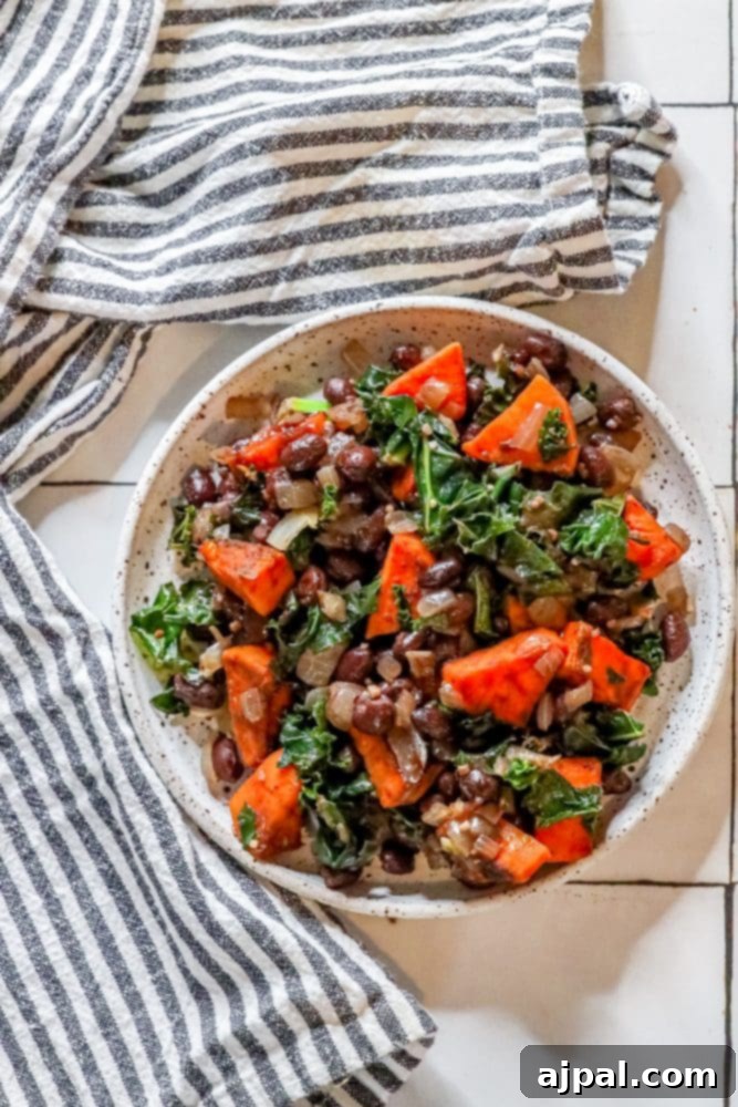 A prepared vegan southwest skillet with sweet potatoes, black beans, and kale, ready for serving on a rustic tile surface.