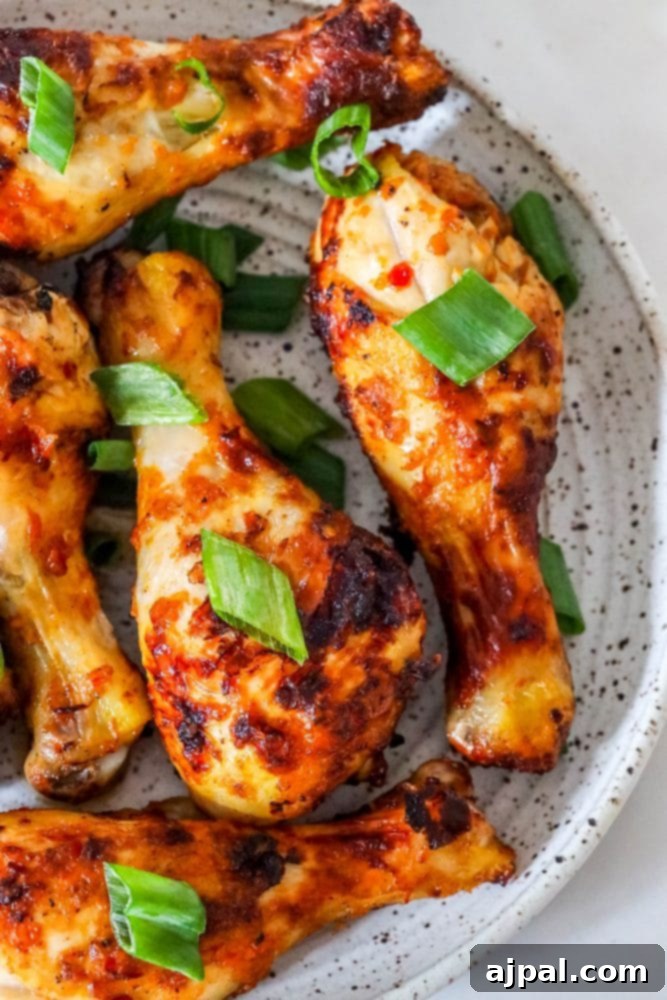 Crispy air-fried piri piri chicken drumsticks garnished with fresh green onions on a rustic white plate.