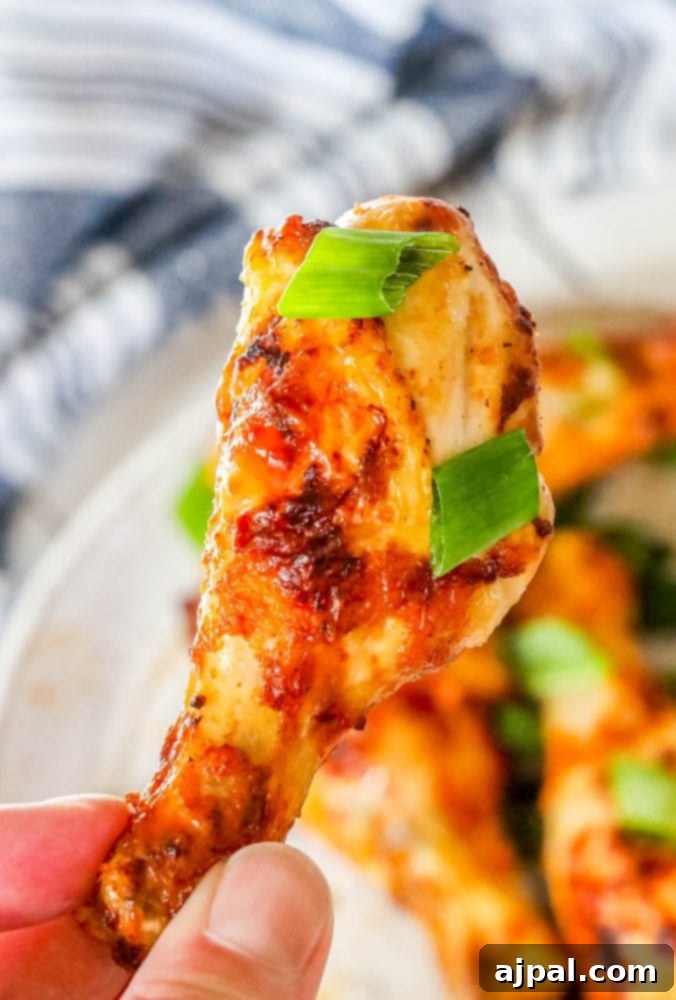 A hand presenting a plate of perfectly air-fried piri piri chicken, garnished with fresh herbs and a vibrant blue napkin.