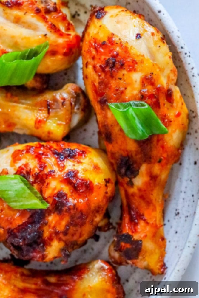 A close-up of air-fried piri piri chicken drumsticks on a white plate, garnished with fresh basil leaves for a vibrant touch.