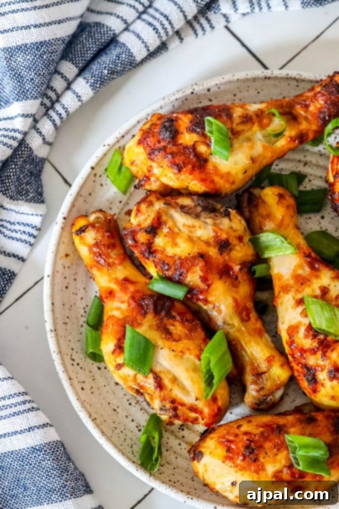 Golden-brown air-fried piri piri chicken wings in a white bowl, topped with vibrant green onions, against a soft blue towel backdrop.