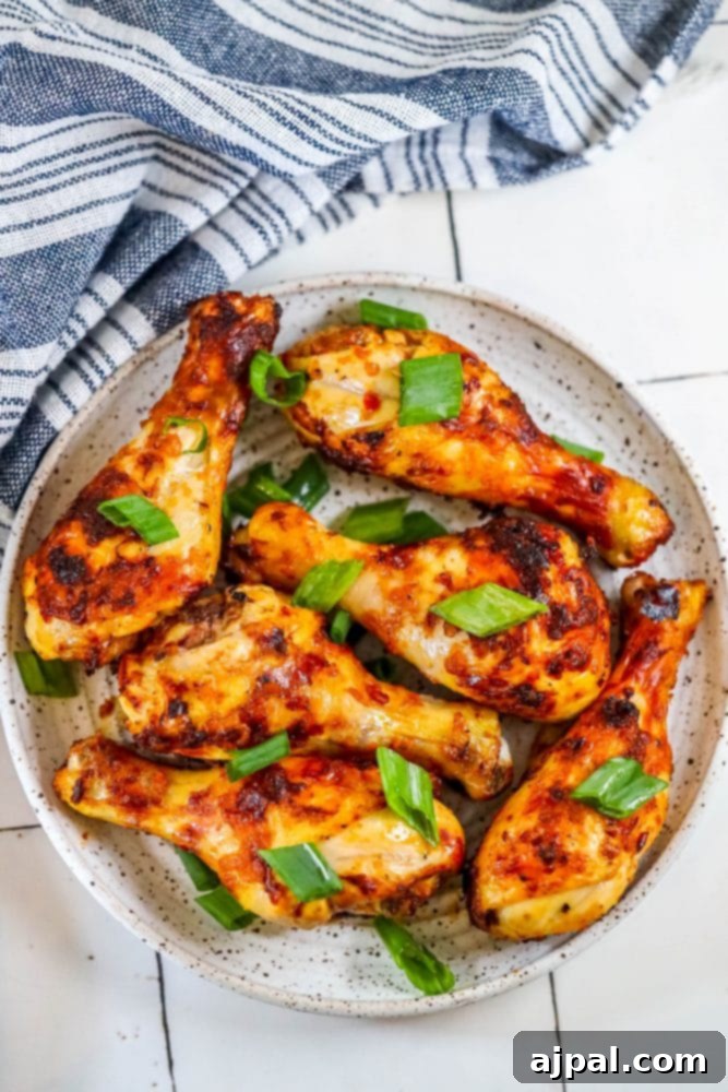 A plate of air-fried piri piri chicken drumsticks garnished with fresh basil leaves, resting on a white plate with a blue napkin in the background.