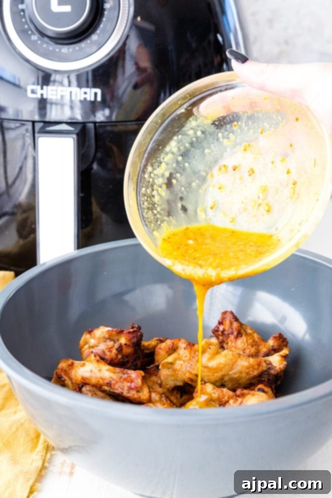 Air Fried Honey Mustard Glazed Wings 10 Honey mustard sauce being poured over crispy chicken wings in a bowl.