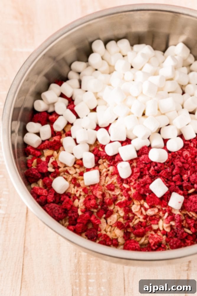 White Chocolate Raspberry Krispie Delights 9 A bowl filled with Rice Krispies cereal, freeze-dried raspberries, and mini marshmallows, ready for mixing.