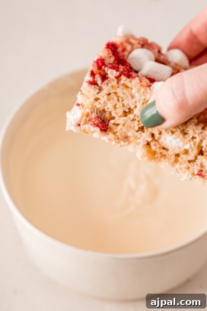 White Chocolate Raspberry Krispie Delights 13 A Rice Krispie treat being carefully dipped into a bowl of melted white chocolate.