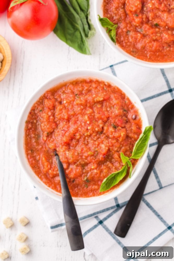 Easy gazpacho soup recipe – two bowls of vibrant tomato soup on a rustic wooden table, garnished with basil.