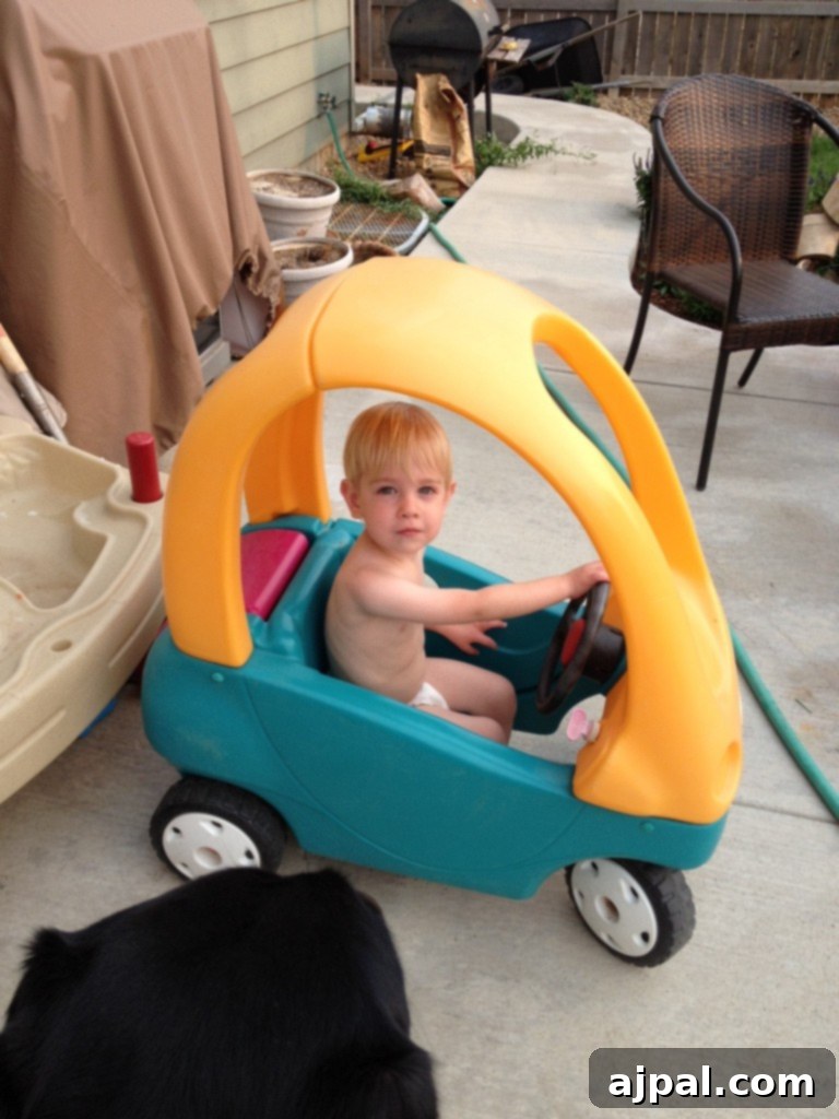 Turn a thrift store Cozy Coupe into an awesome Batmobile! Picture of a toddler in a plastic Cozy Coupe car, soon to be a custom Batmobile, alongside a dog