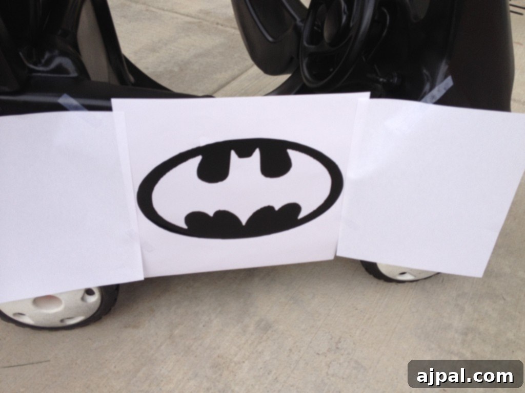 How to make a Batmobile stencil using a cutting machine Picture of a black-painted Cozy Coupe car with a paper stencil of the Batman logo taped over it, ready for the yellow accent