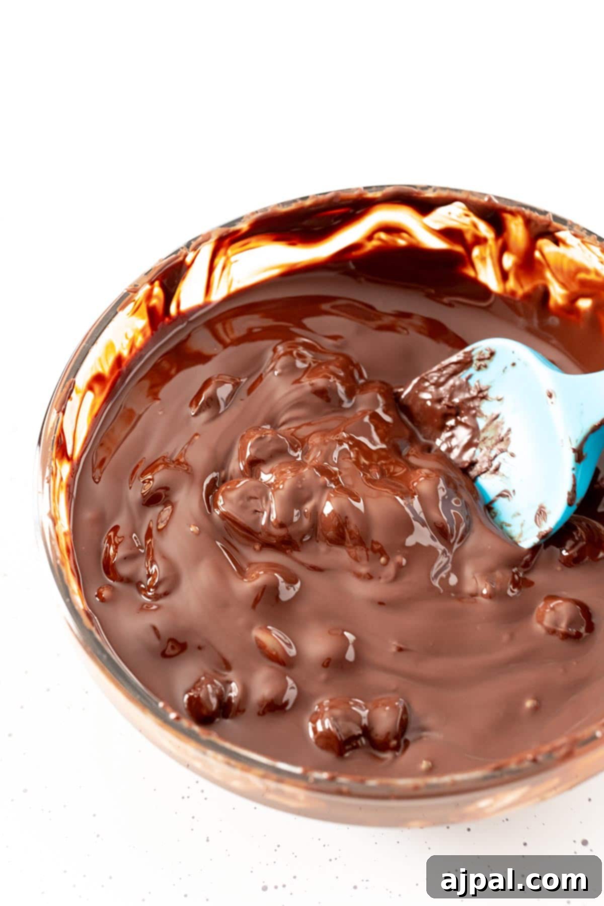 Decadent Peanut Butter Hot Cocoa Bombs 11 Clumpy chocolate in a bowl being stirred, illustrating the initial stages of melting chocolate.
