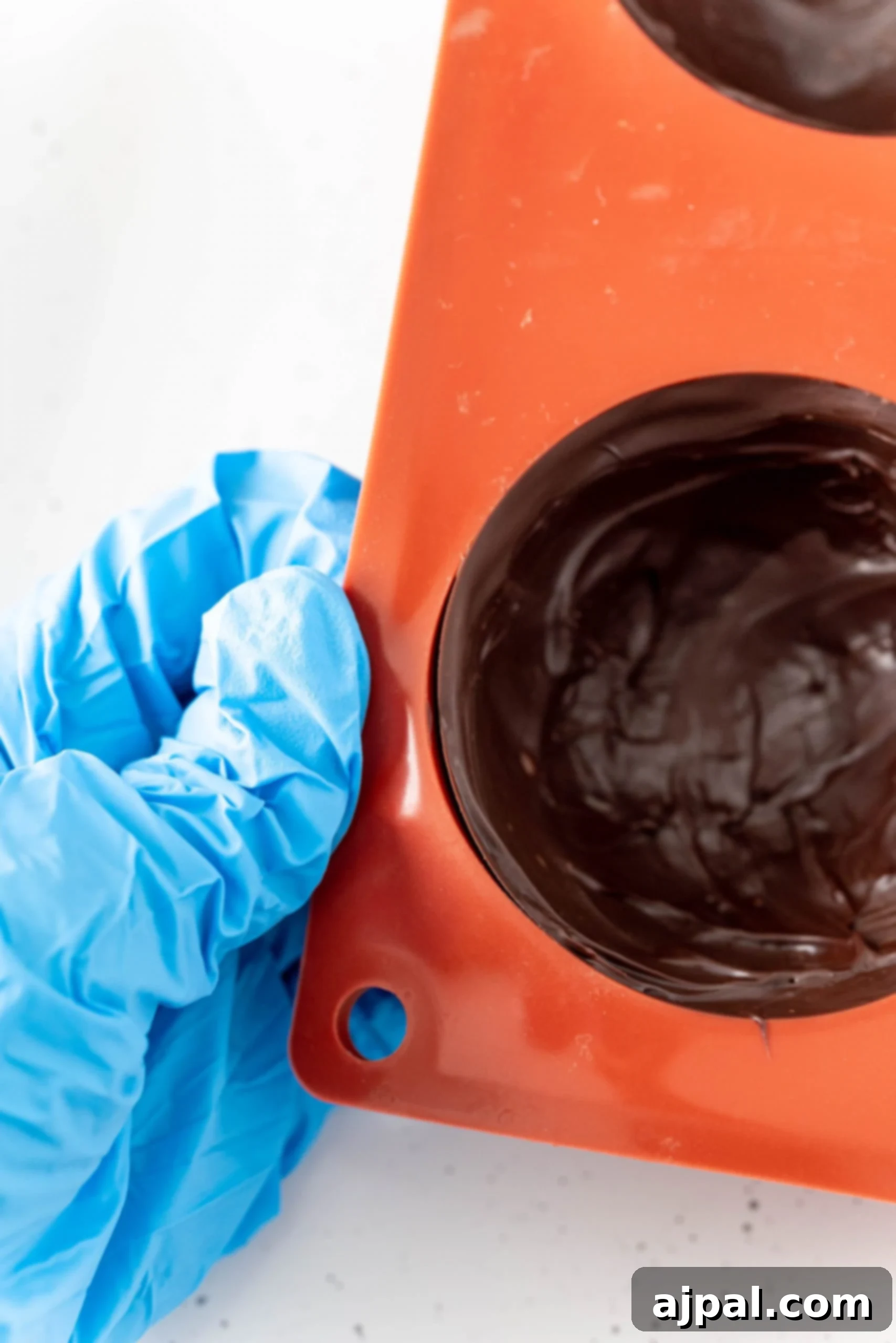 Decadent Peanut Butter Hot Cocoa Bombs 14 Glove holding an orange mold covered in chocolate, illustrating the careful handling required.