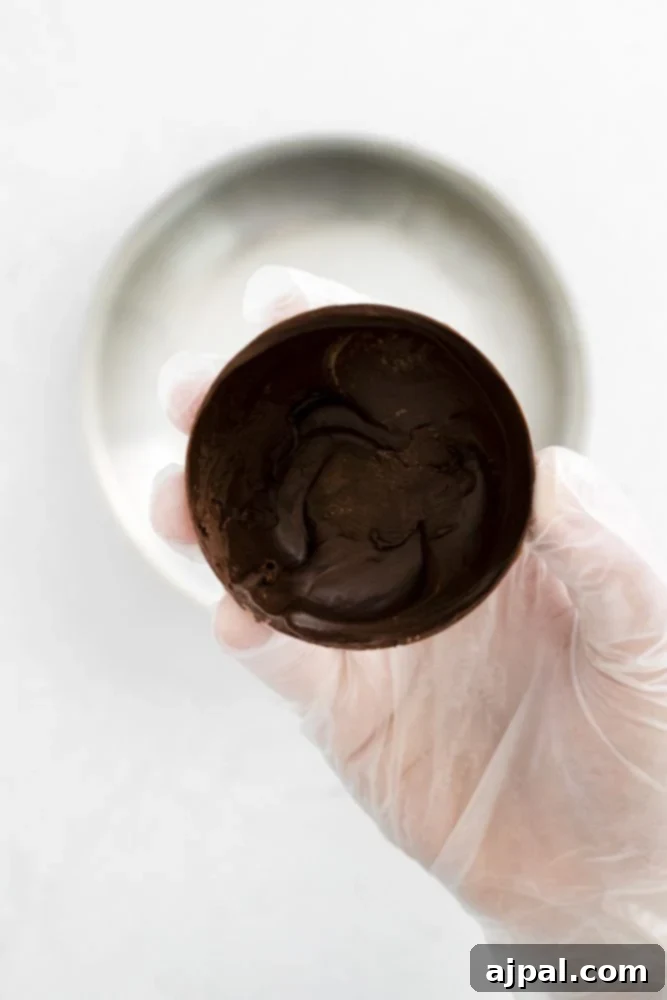 Decadent Peanut Butter Hot Cocoa Bombs 19 Gloved hand holding a chocolate sphere with a pan in the background, demonstrating the sealing process.