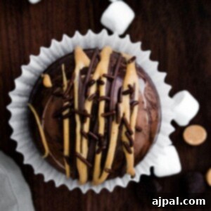 A peanut butter hot chocolate bomb-inspired chocolate cupcake with marshmallows and chocolate drizzle.