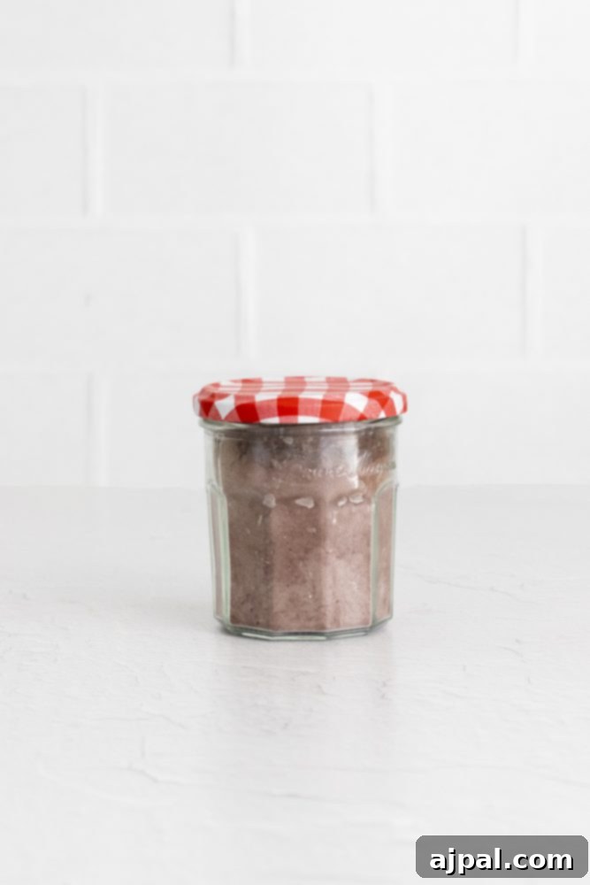 Decadent Peanut Butter Hot Cocoa Bombs 6 Brown hot chocolate mix in a glass jar with a checkered top, a key ingredient for hot cocoa bombs.
