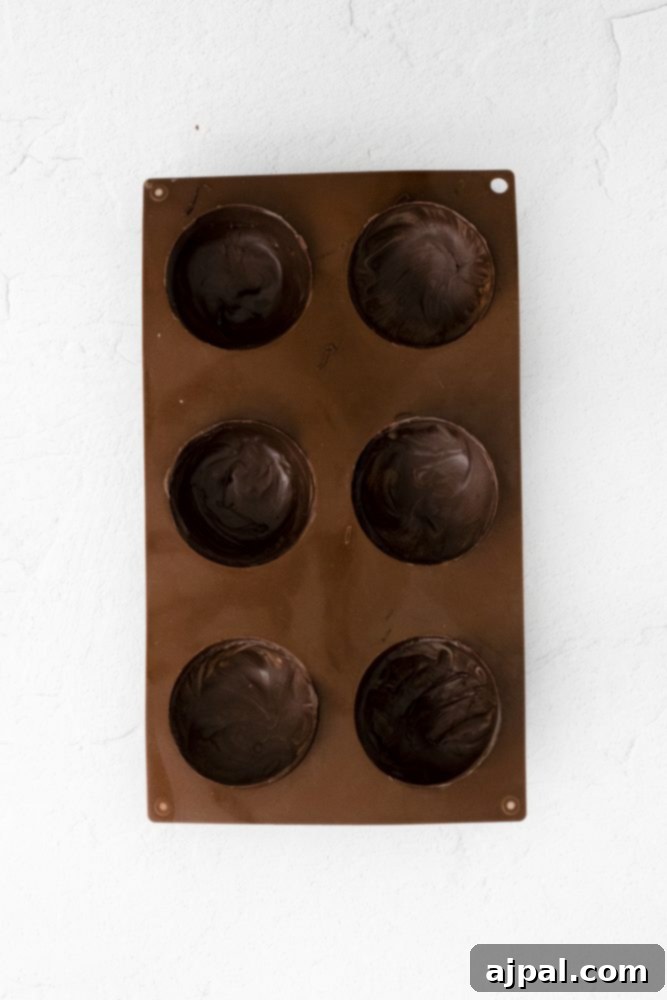 Decadent Peanut Butter Hot Cocoa Bombs 7 Brown silicone mold with chocolate in the cups, demonstrating the initial step of making chocolate shells.