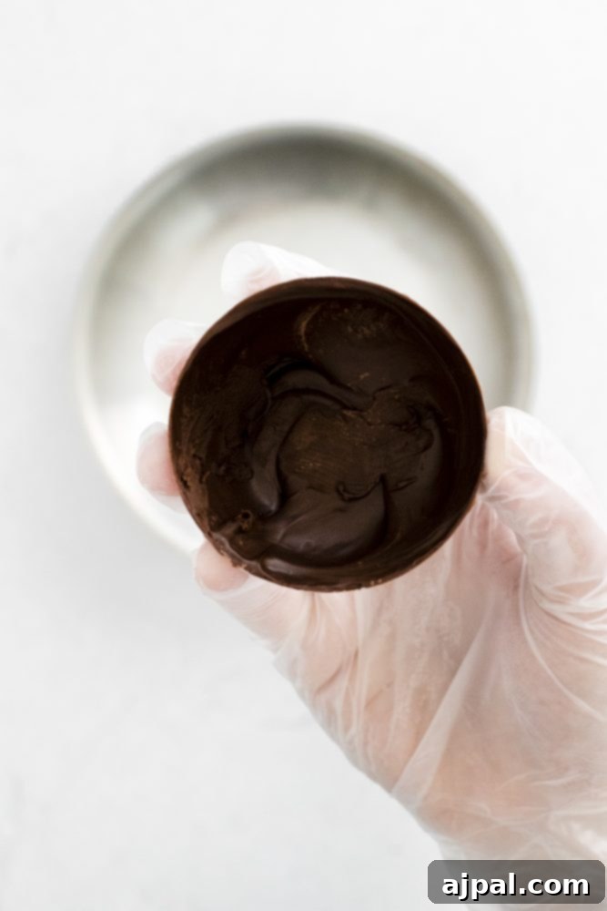 Decadent Peanut Butter Hot Cocoa Bombs 8 Gloved hand holding a chocolate sphere with a pan in the background, showing the careful handling of the chocolate shells.