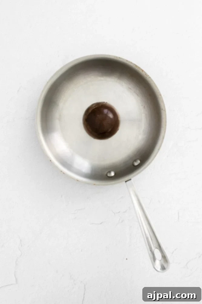 Decadent Peanut Butter Hot Cocoa Bombs 9 Chocolate sphere in a stainless steel pan, highlighting the process of sealing the hot cocoa bombs.