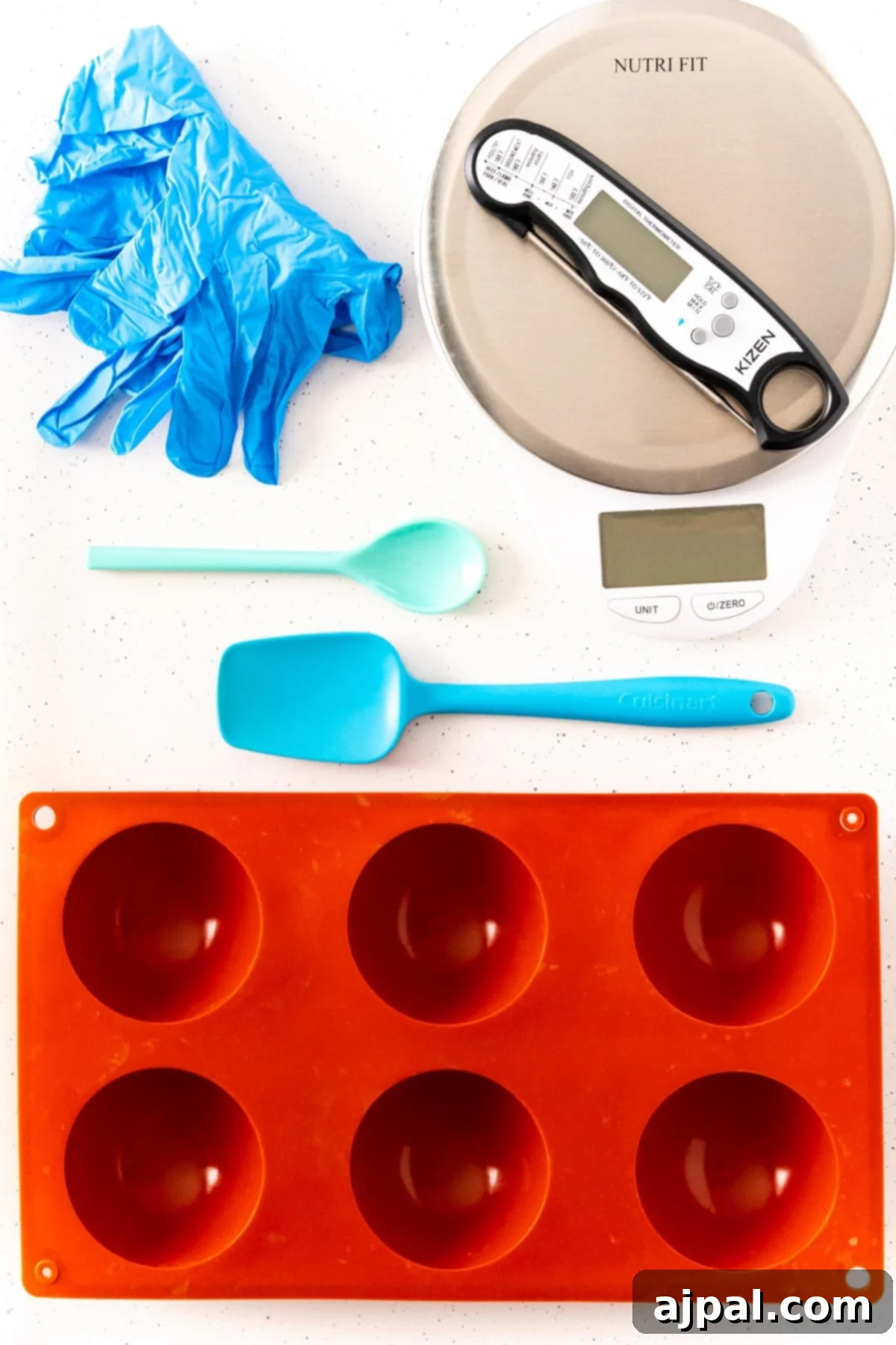 Decadent Peanut Butter Hot Cocoa Bombs 10 Silicone mold, gloves, spatula, spoon, temperature gauge, and other tools laid out for making hot chocolate bombs.