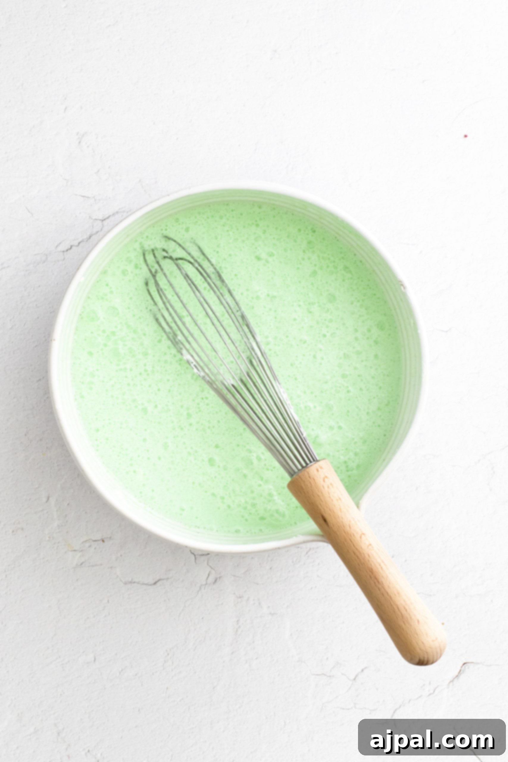 A bowl of layered green jello with a whisk in it.