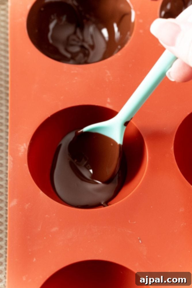 Berry Burst Hot Cocoa Spheres 9 Chocolate being spooned into an orange silicone mold.