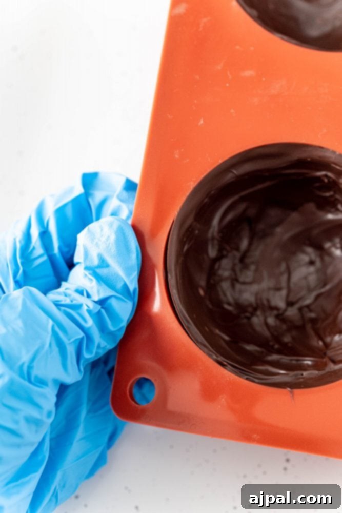 Berry Burst Hot Cocoa Spheres 10 Gloved hand holding an orange silicone mold covered in chocolate.