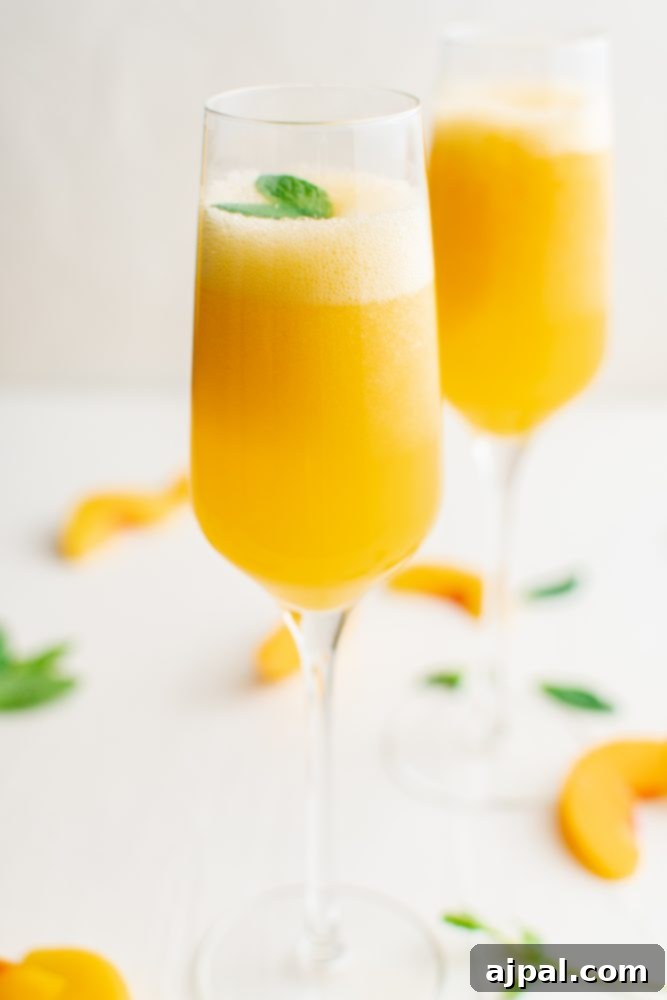 Two champagne glasses filled with vibrant peach bellinis, garnished with fresh mint leaves, set against a soft, bright background.