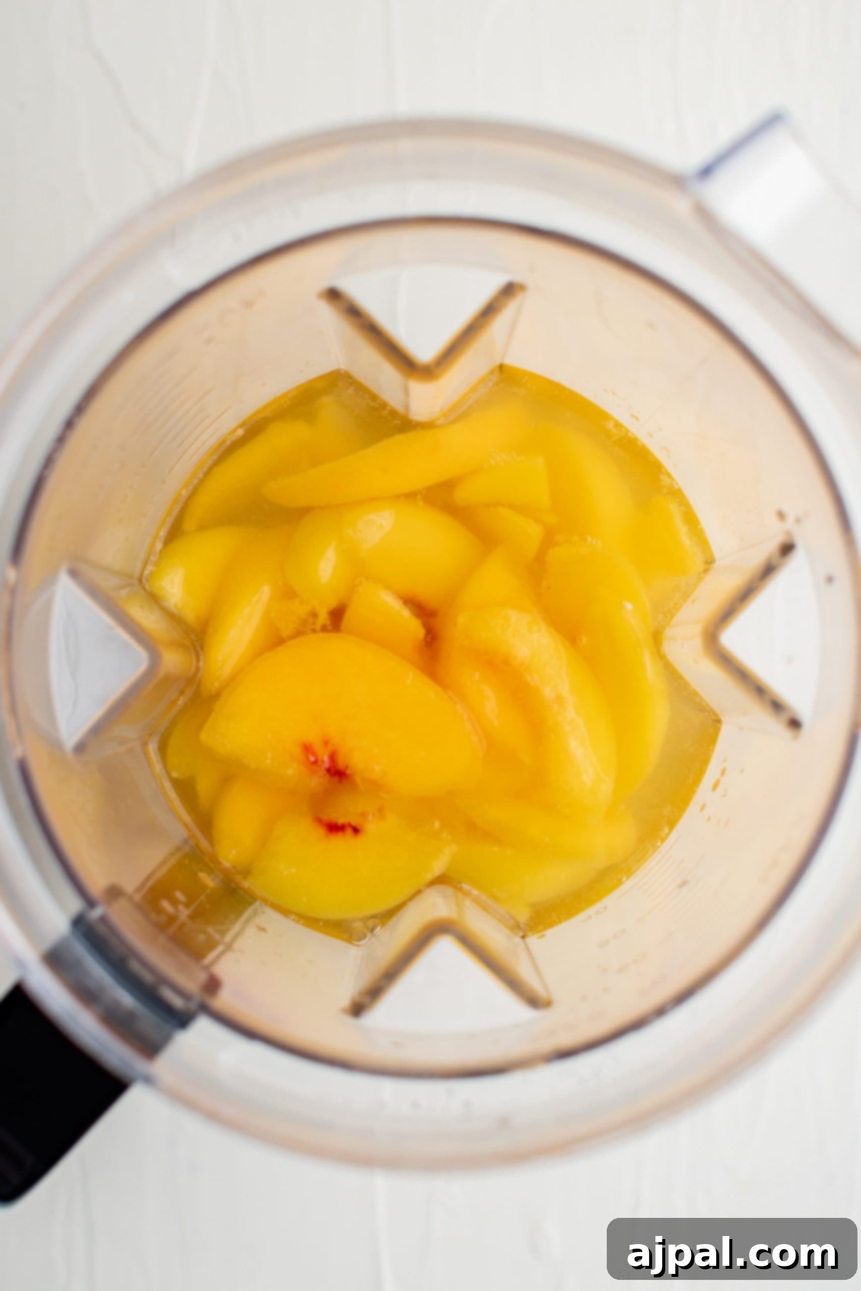 Frozen peach slices, simple syrup, peach nectar, and lemon juice being blended in a large blender for the Bellini puree.