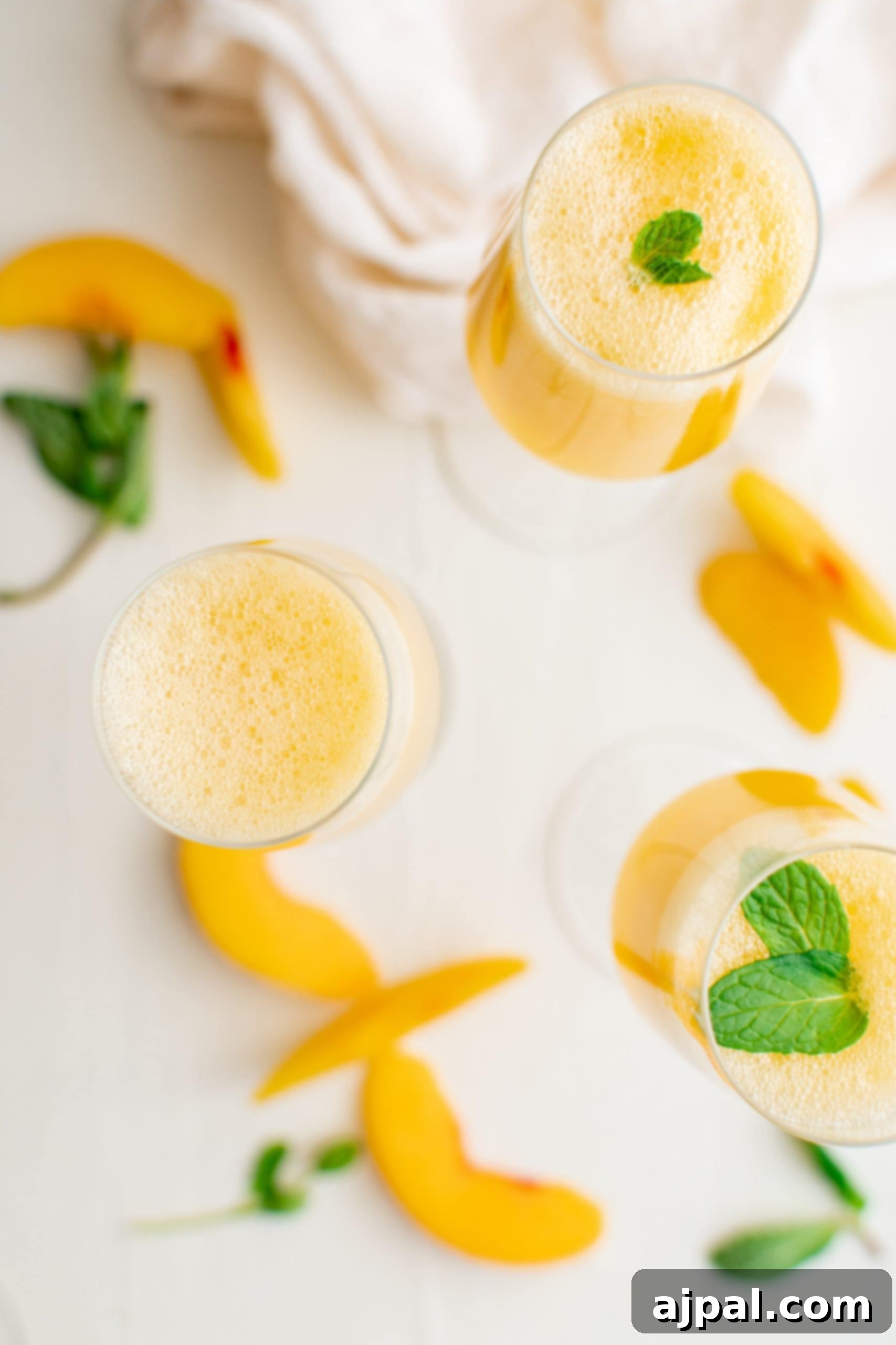 A single elegant champagne glass filled with a peach bellini, garnished with a vibrant mint leaf, set against a blurred light background.