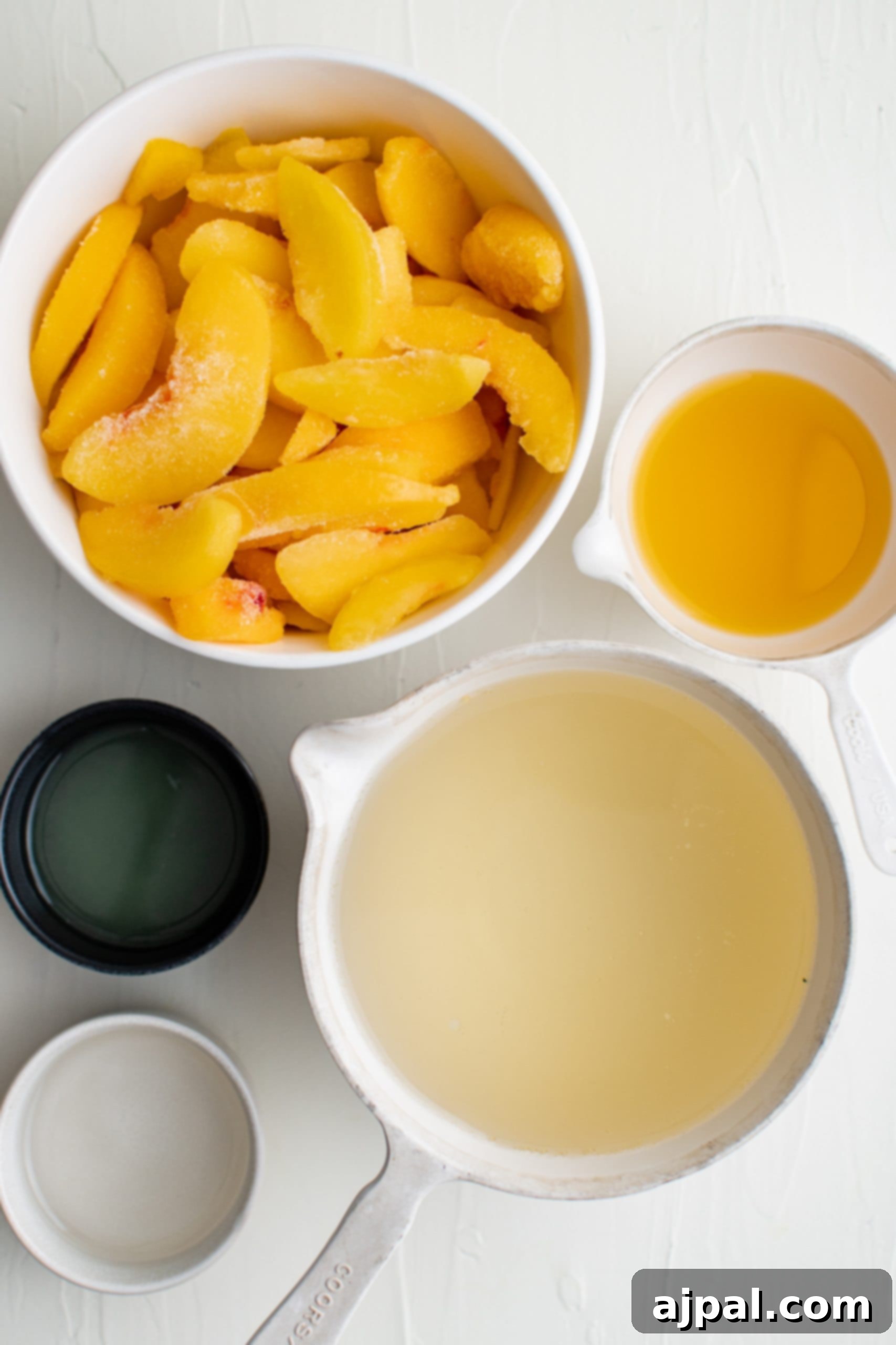 A flat lay of Bellini ingredients: frozen peach slices, a bottle of champagne, a small bowl of simple syrup, and loose sugar.
