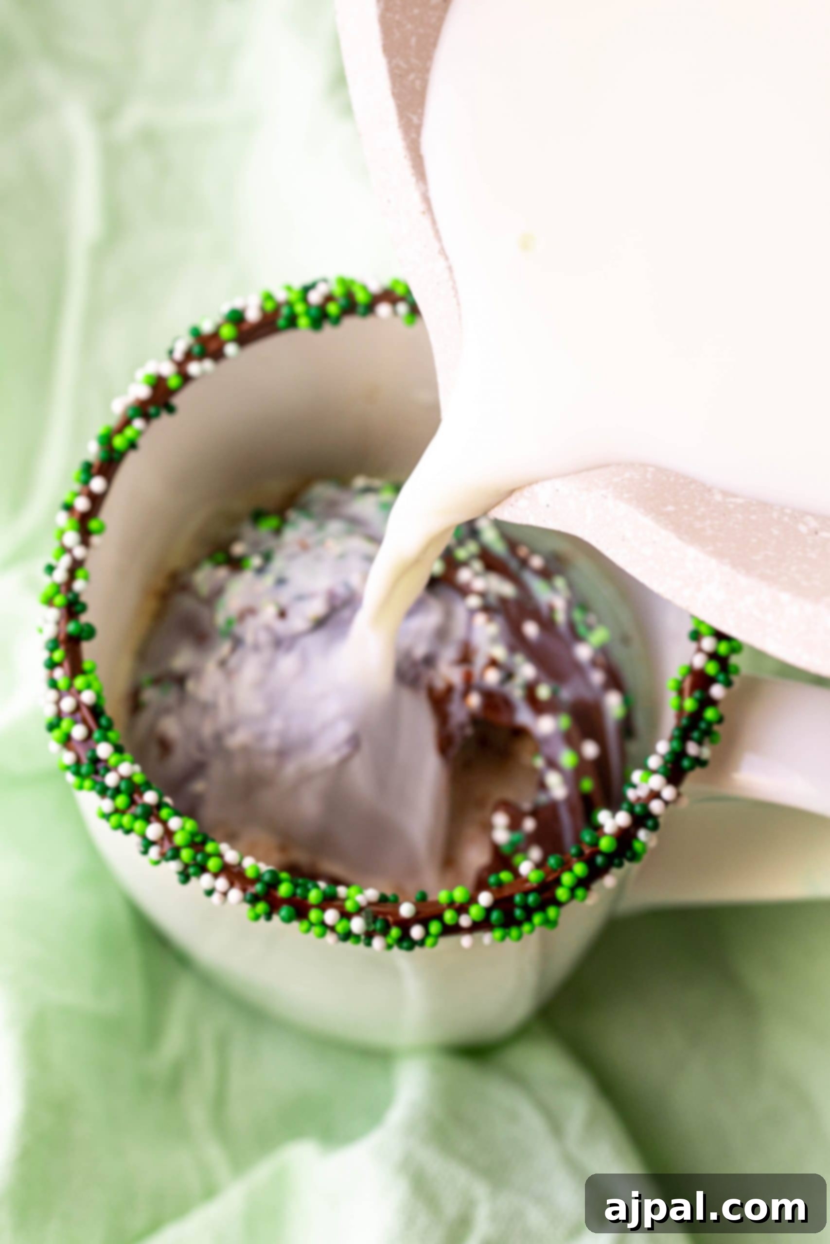 Irresistible Mint Hot Chocolate Bombs 14 milk being poured into a mug with hot chocolate bomb in it, sprinkles on the rim.