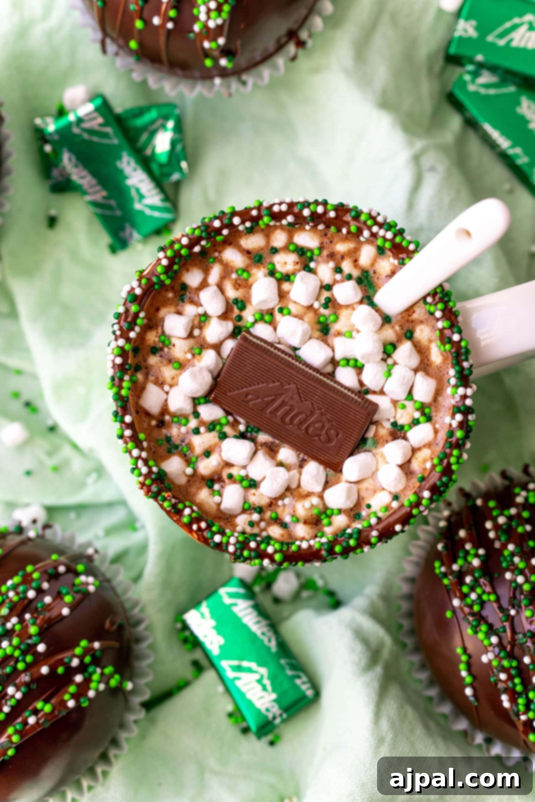 Irresistible Mint Hot Chocolate Bombs 15 mint hot chocolate in a white mug with an andes mint on it and green sprinkles.