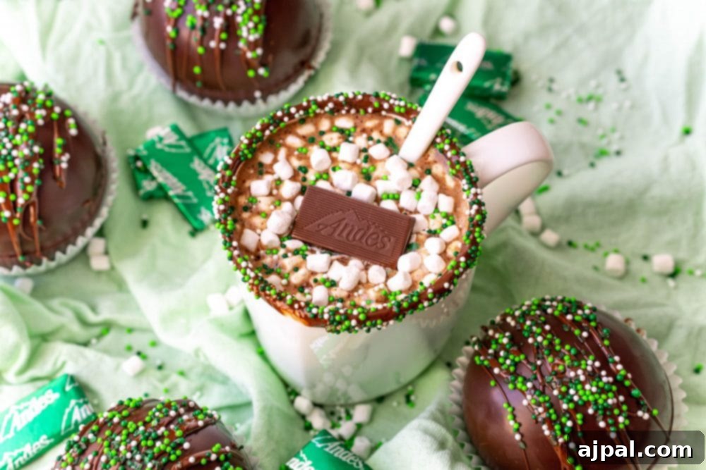 Irresistible Mint Hot Chocolate Bombs 3 hot chocolate with green sprinkles on the edge with an Andes mint and marshmallows int it and a spoon