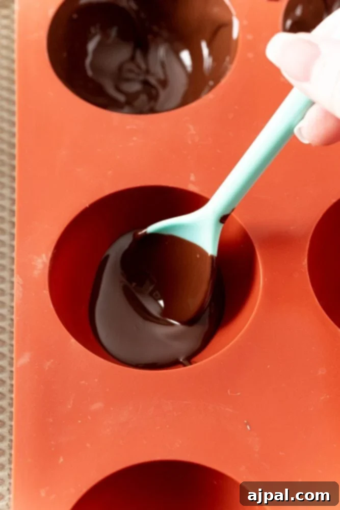 Irresistible Mint Hot Chocolate Bombs 7 orange mold with chocolate being spooned in.