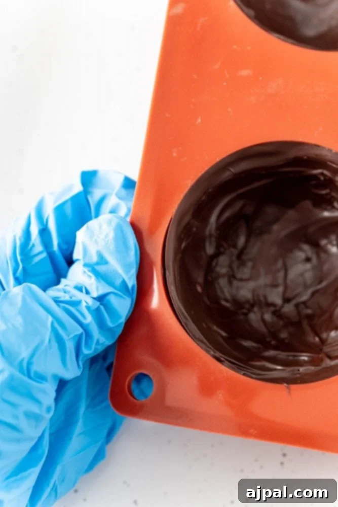 glove holding orange mold covered in chocolate