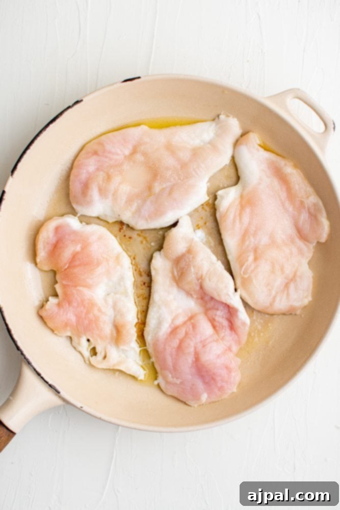 Creamy garlic chicken breasts being cooked in a skillet.