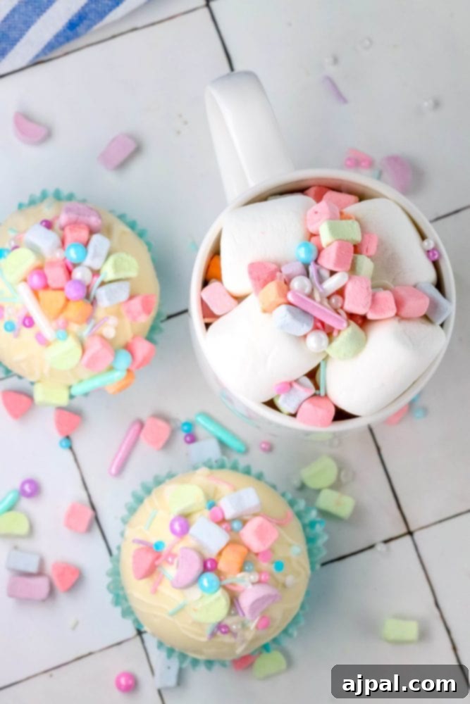 Magical White Chocolate Lucky Charms Bombs 2 white chocolate hot chocolate bomb in a blue cupcake wrapper with lucky charms marshmallows and sprinkles on top next to a mug with cocoa, sprinkles, and marshmallows in it