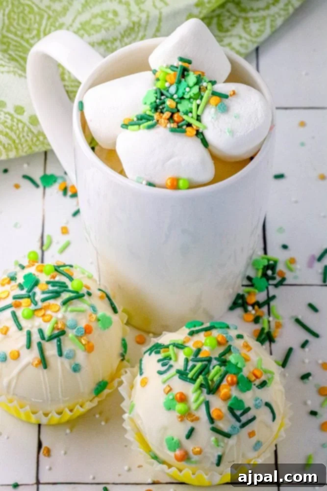Lucky Green Saint Patrick's Hot Chocolate Bombs 2 white chocolate hot chocolate bombs covered in saint patricks day sprinkles on a table next to a mug with marshmallows and green and gold sprinkles in it