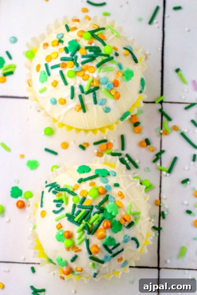 Lucky Green Saint Patrick's Hot Chocolate Bombs 5 white chocolate hot chocolate bombs covered in saint patricks day sprinkles on a table next to a mug with marshmallows and green and gold sprinkles in it