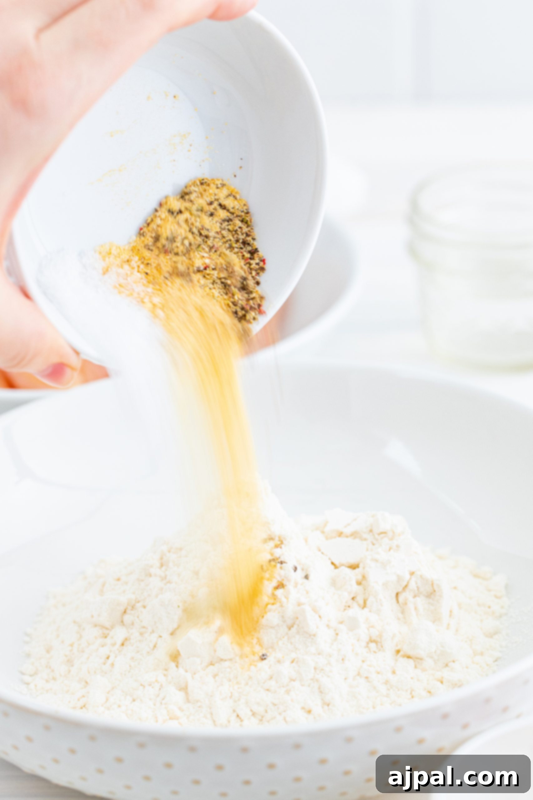 A hand pouring flour into a bowl, preparing ingredients for chicken tenders.