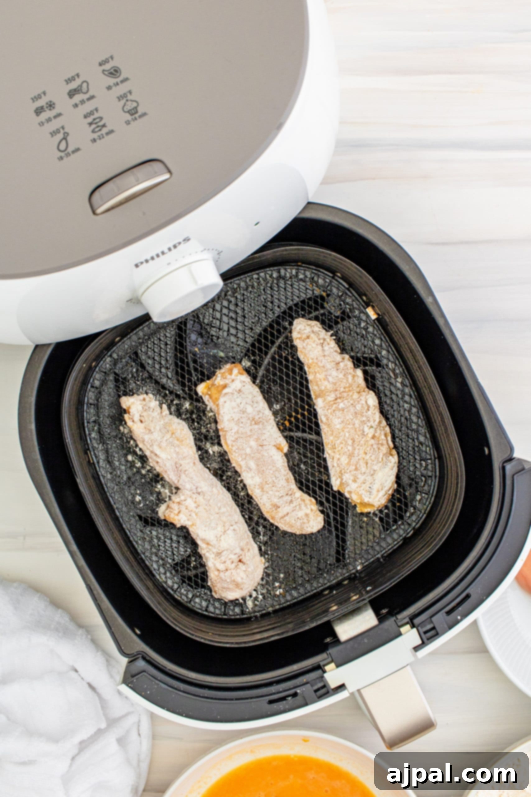 An air fryer basket filled with perfectly cooked chicken tenders and roasted vegetables.