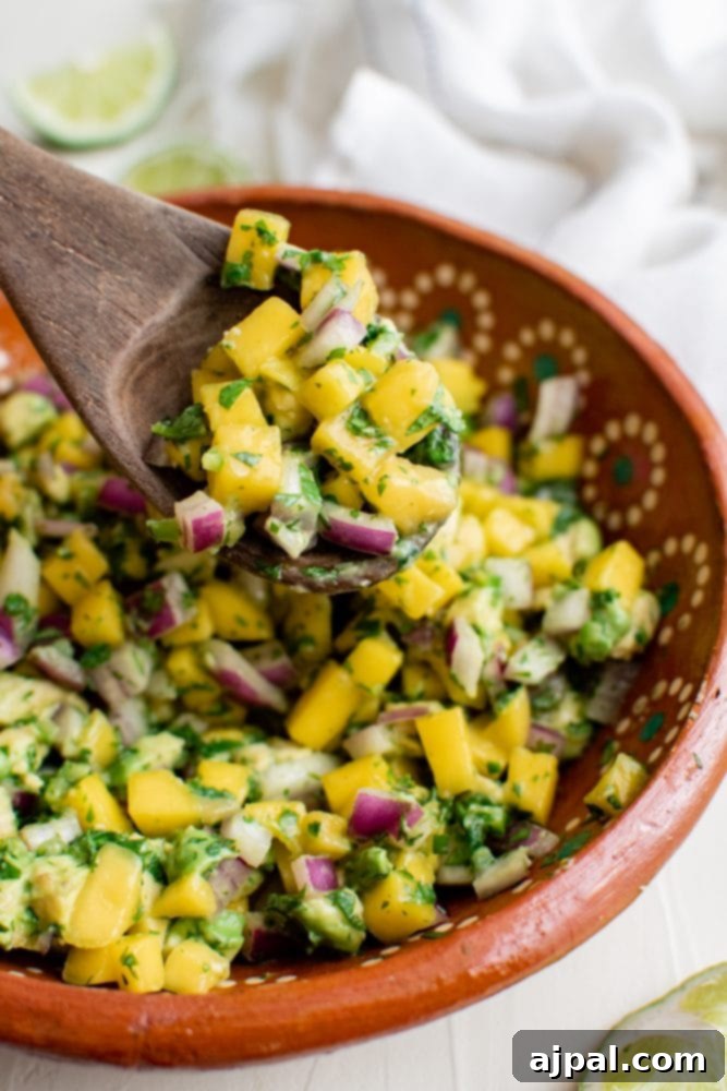 Tropical Mango Avocado Salsa 3 A ceramic bowl filled with freshly made easy mango avocado salsa, with a wooden spoon resting invitingly in it.